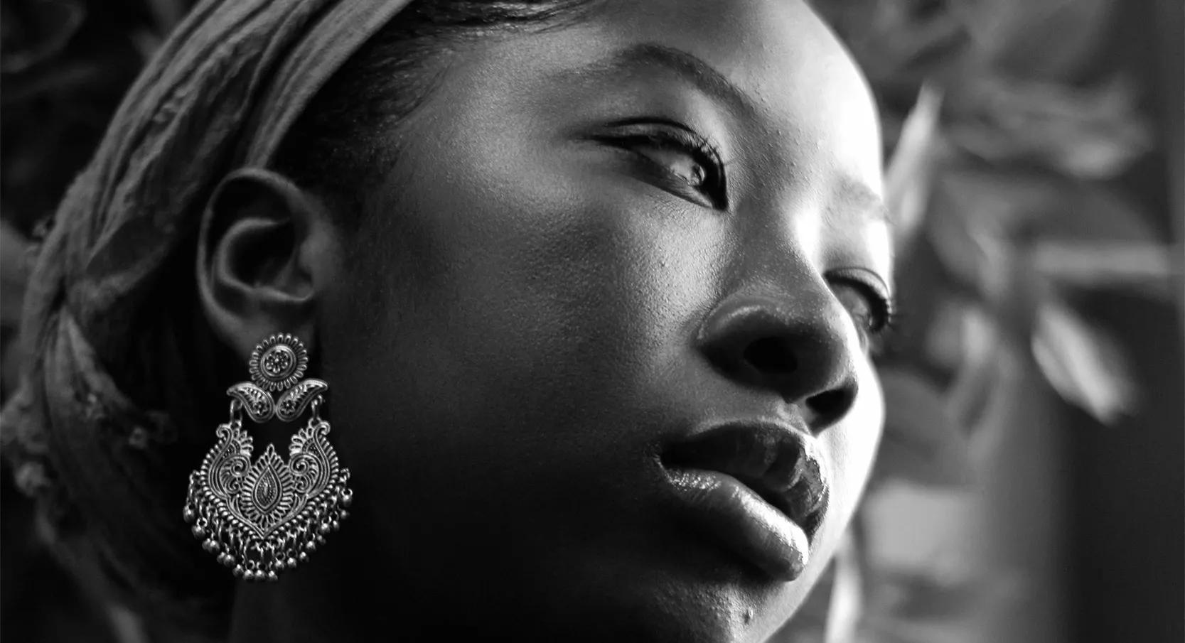 A woman with a gold earring and hairband, her head tilted to the side. 