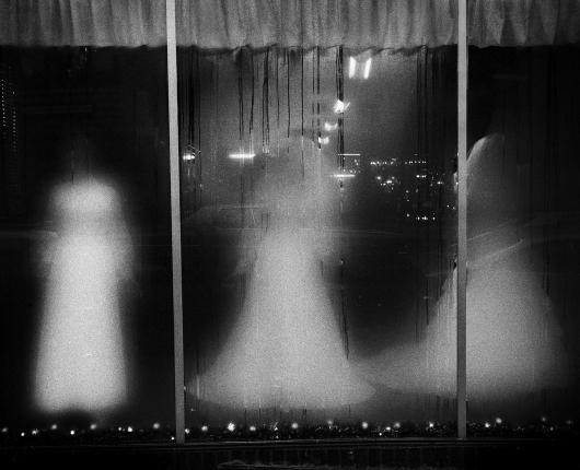 Three ghostly mannequins standing in a fogged up display window. 