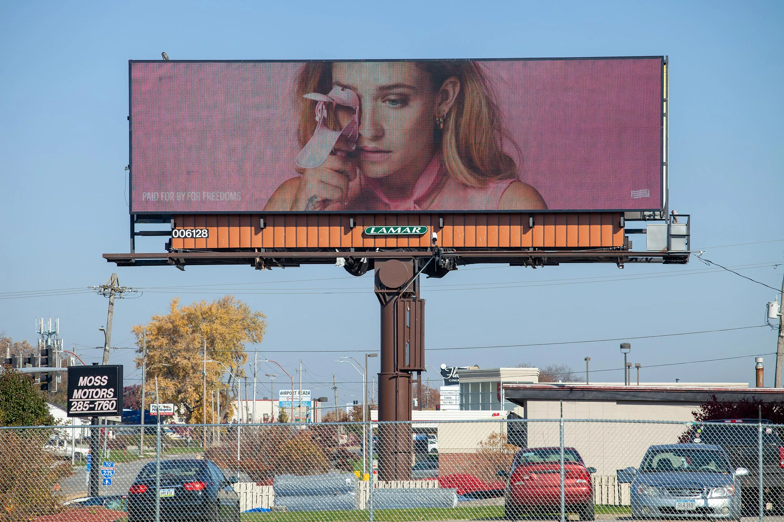 A billboard above a busy highway with a woman looking through a speculum. 