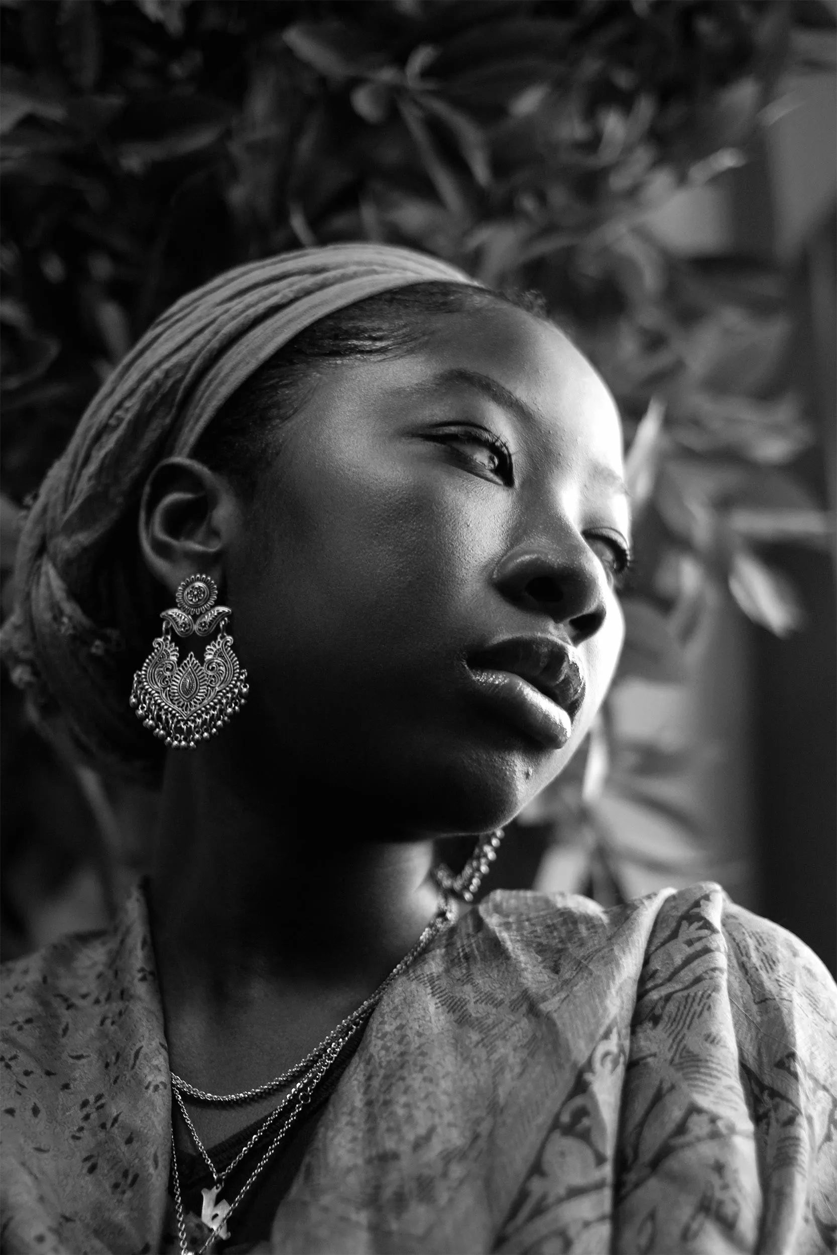 A woman with a gold earring and hairband, her head tilted to the side. 