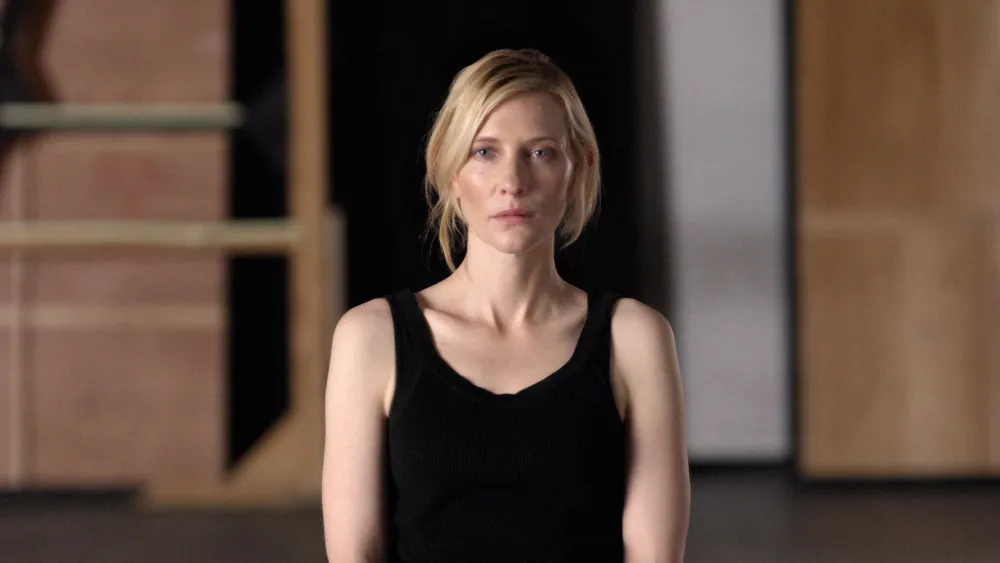 A woman in a plain black dress staring at the camera. 