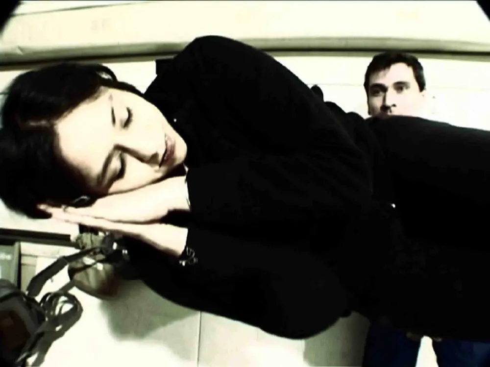 A woman sleeping on her side while a man in the background looks onward. 