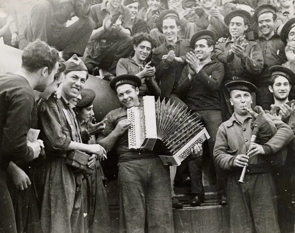 Navy cadets playing music while a crowd of cadets cheer them on.