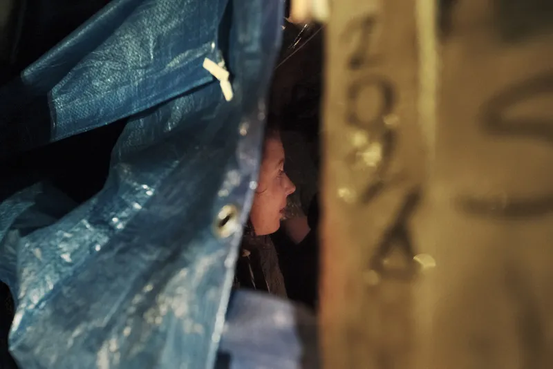 The side profile of a young woman inside a makeshift tarp tent. 