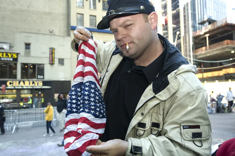A man winking at the camera, holding the American flag in his hand. 