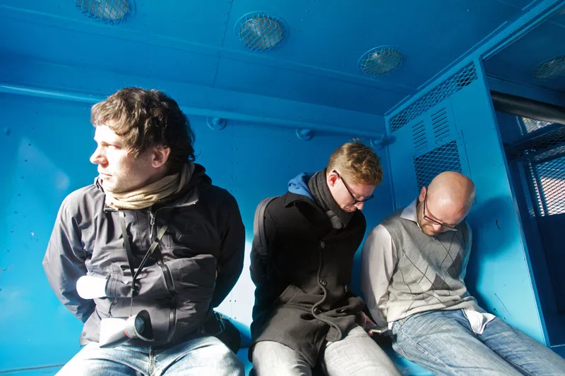 Three men detained in the back of a police truck. 