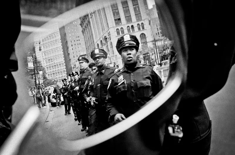 A row of policemen, as seen through the reflection of a motorcycle mirror. 