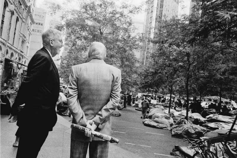 Two old men in suits with their hands behind their backs. 