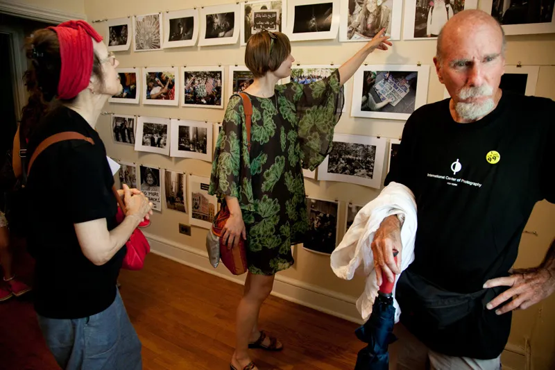 A few people pointing at a photo hung up on the wall of a photography exhibition. 