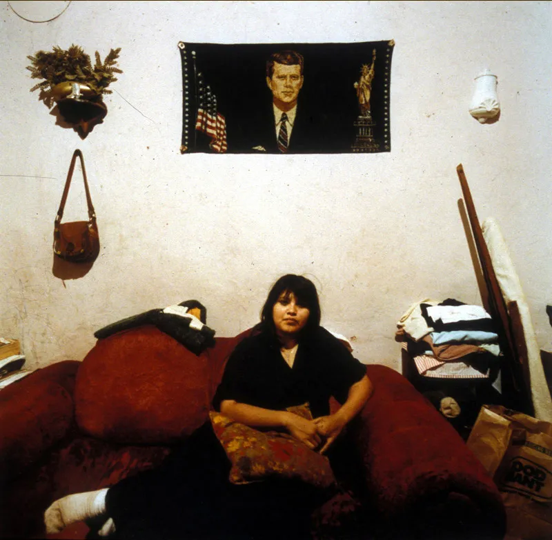 A woman laying on her couch with a embroidered picture of JFK hanging on the wall behind her.
