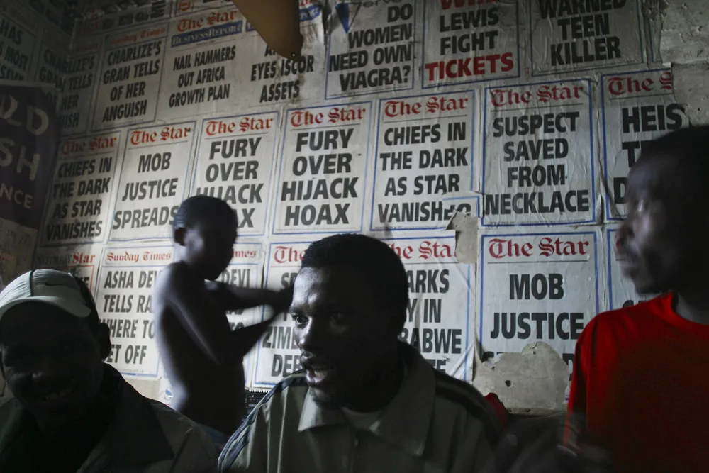 Three men talking among themselves, while a boy behind them stands in front of a wall entirely covered with ladies from The Star newspaper.