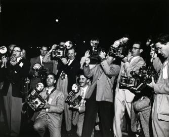 Black and white photograph of a group of photographers with their cameras at a premiere