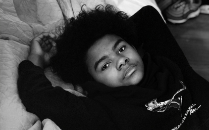 Two children laying in a bed, the younger sister is asleep while the older brother is looking at us.