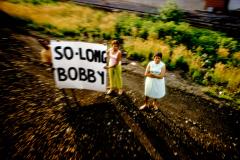 Three women with a sign that says "So Long Bobby". 
