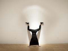 An individual in all black doing a handstand in an art gallery. 