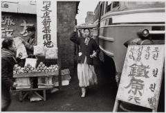 An old photo of a lady carrying food on her head.