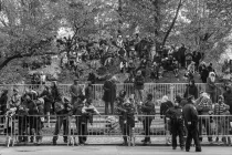 A large crowd sitting on rocks and leaning against a police barricade watching something out of frame.