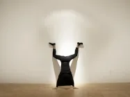 An individual in all black doing a handstand in an art gallery. 