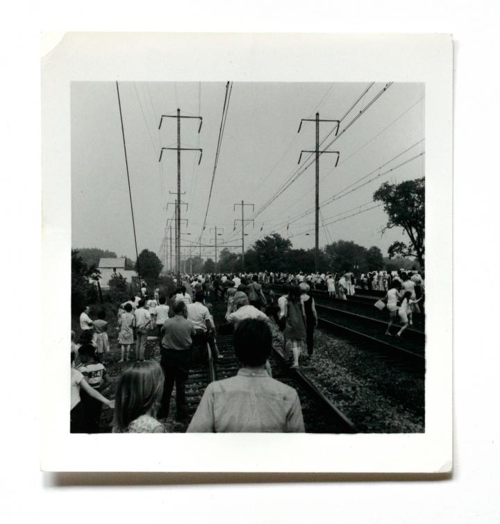 An antique photo of people standing on train tracks.