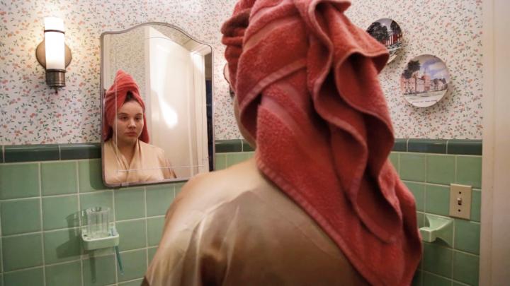 A girl looking into a bathroom mirror.