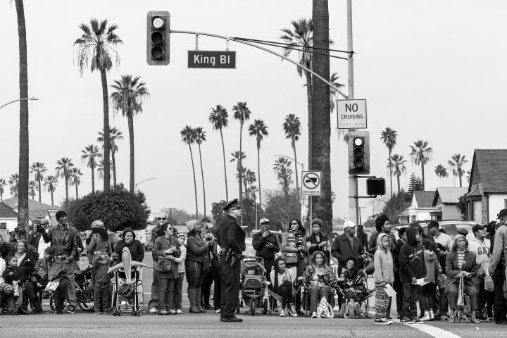 A row of people on the intersection of Kings Blvd watching something out of frame. 