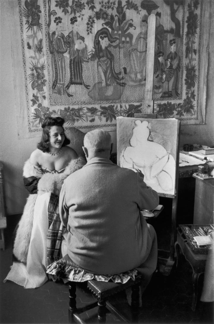 The backside of an artist drawing a woman in a regal fur coat. 