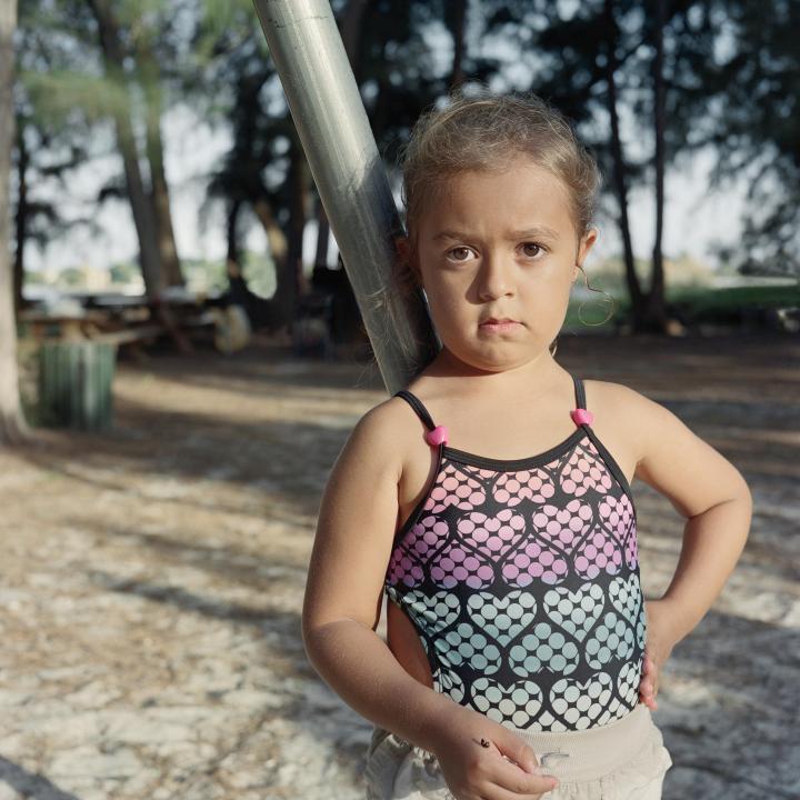 A young girl seriously posing for the camera with a hand on her hip in the middle of a park. 