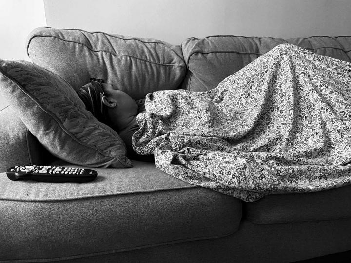 A woman sleeping on the couch with a blanket, the TV remote by her side. 