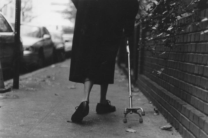 The lower half backside of an old woman with a cane walking down the street. 