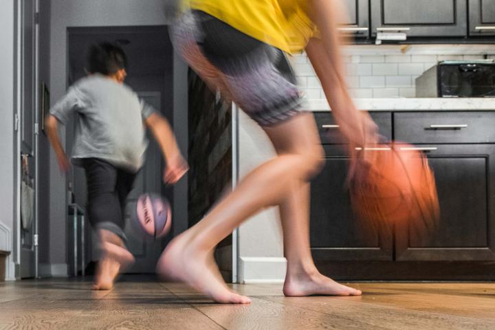 A blurry action shot of two kids in a kitchen dribbling basketballs. 