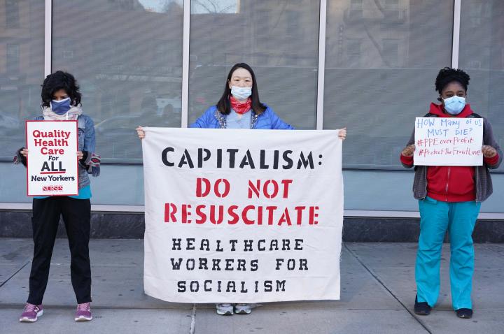Three protesters with signs protesting for socialism and healthcare for all. 