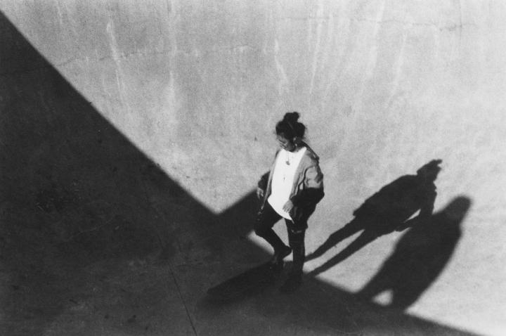 A black and white image of a woman inside a empty pool, skateboarding. 