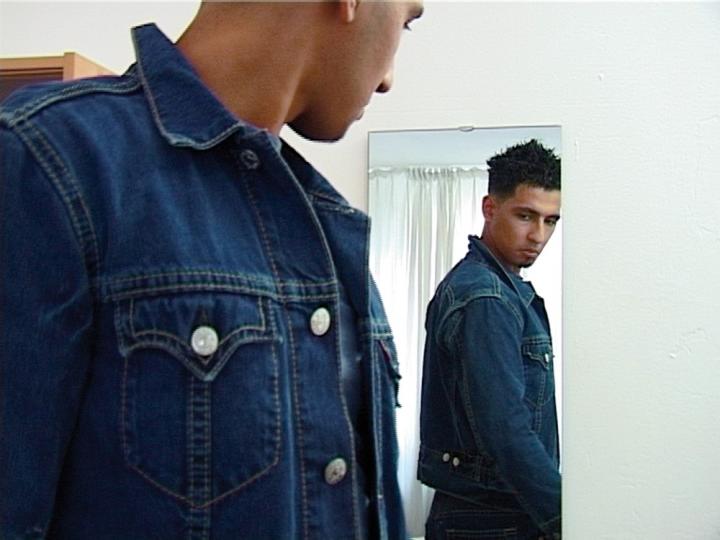 A man checking out his denim jacket in the mirror. 