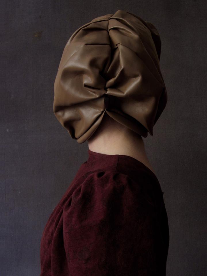 A side profile of someone in a dress, the head covered in a leather mask. 