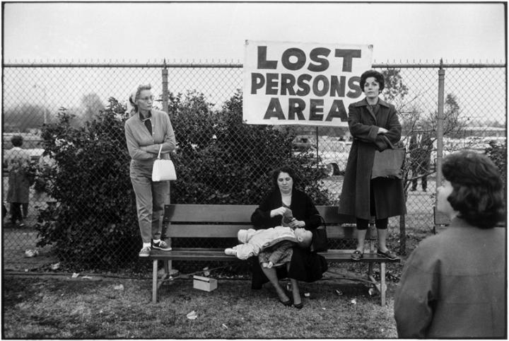 Three women on a bench, with a sign in the background saying "Lost Persons Area".