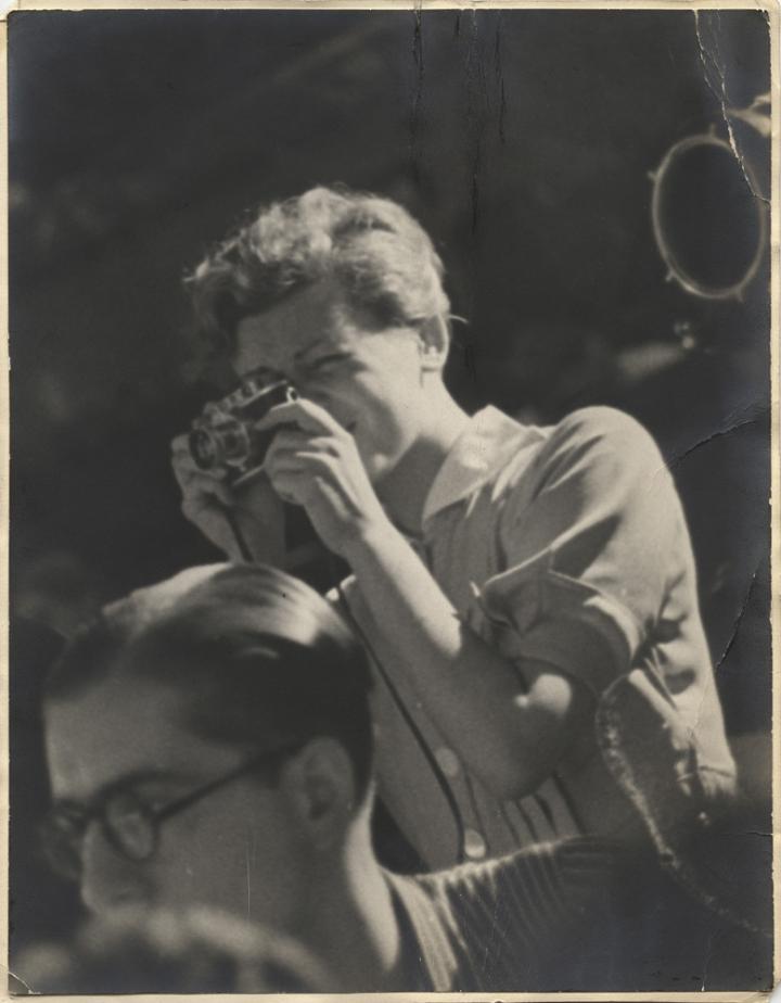 An antique photo of a woman taking a picture.