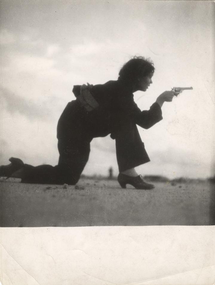 A woman crouched, looking through the ironsight of a revolver. 
