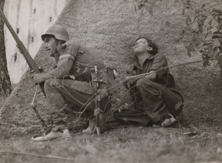 Soldiers crouching behind a rock under fire. 
