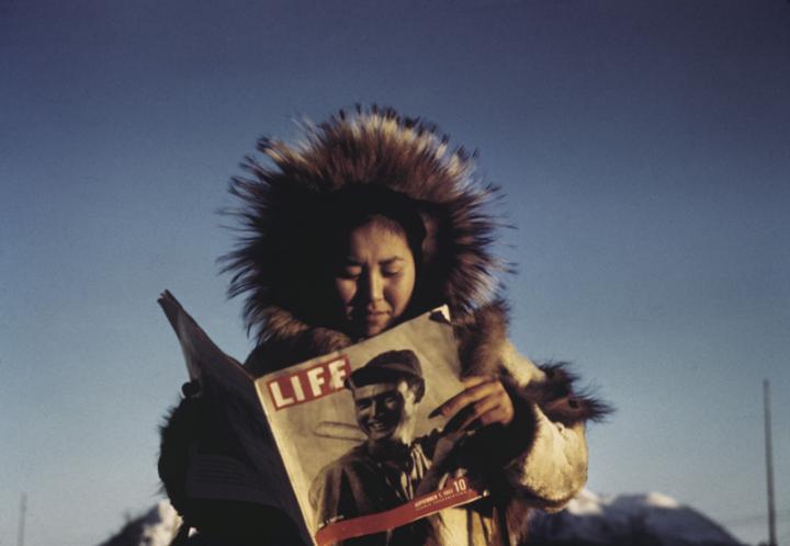 An Inuit in their native coat reading Life magazine. 