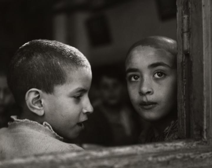 Two children with shaved heads in the windowsill of a damaged building. 