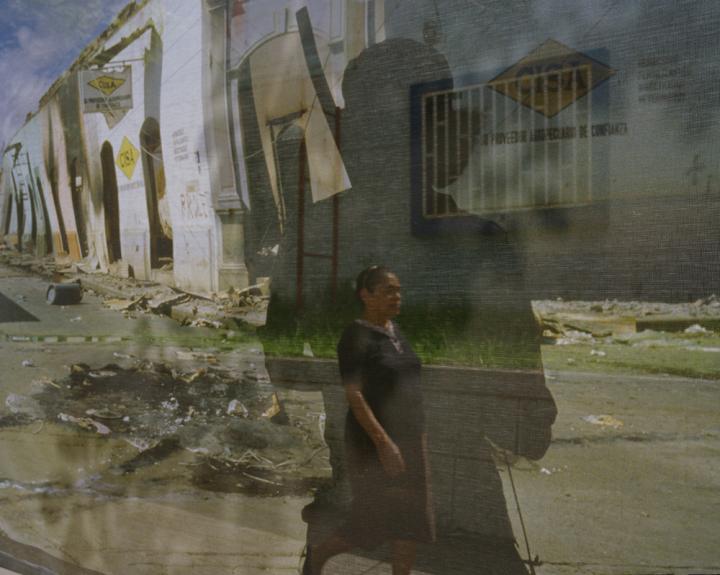 A double exposure shot, with a woman walking down a destroyed city street and her body being engulfed in the silhouette of a soldier.