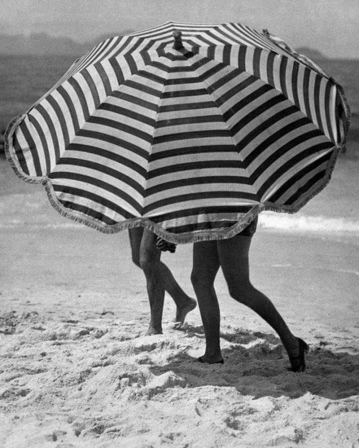 Two beachgoers hidden behind their umbrella on the beach.