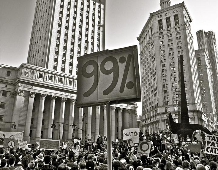 A crowd of protestors and a sign in the foreground, "99%".