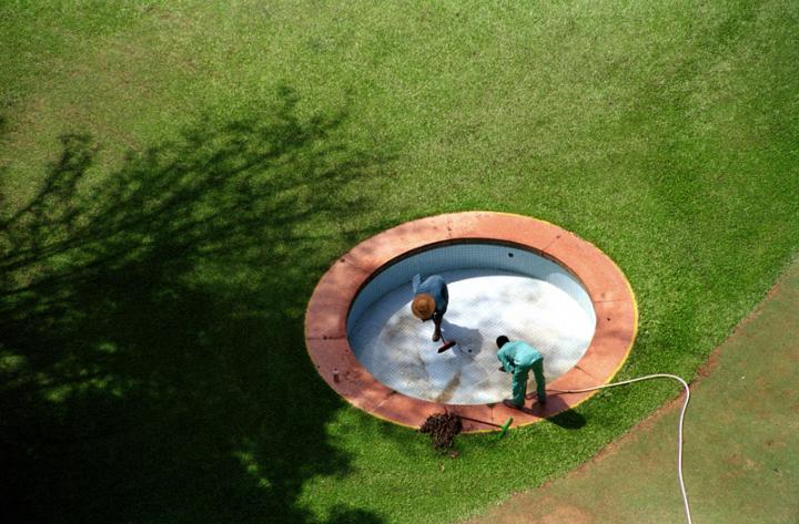 Two people cleaning out the inside of a empty pool, as seen from above. 