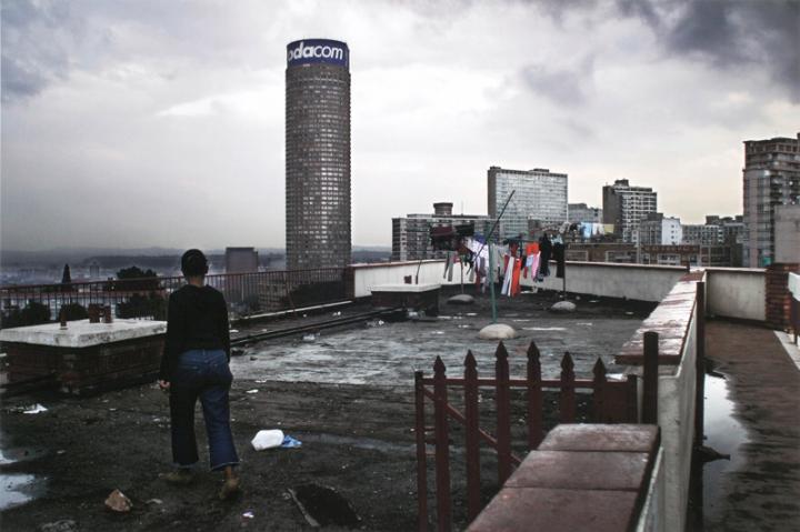 The roof of a grey building, with someone walking to the edge where colorful clothes were hung up to dry.  