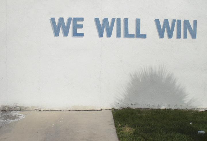 The words "We Will Win" written on the side of a light blue building. 
