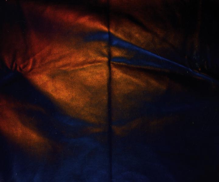 A black leather sheet wrinkled, shining with blue and orange lights. 