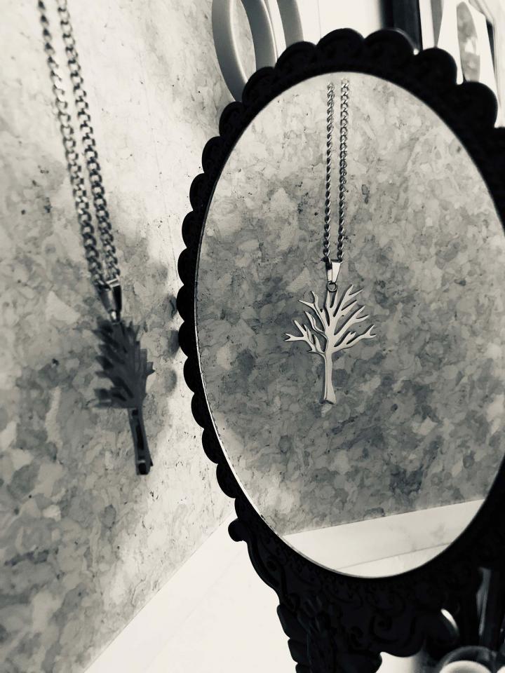 A tree pendant dangling in the reflection of a victorian mirror. 