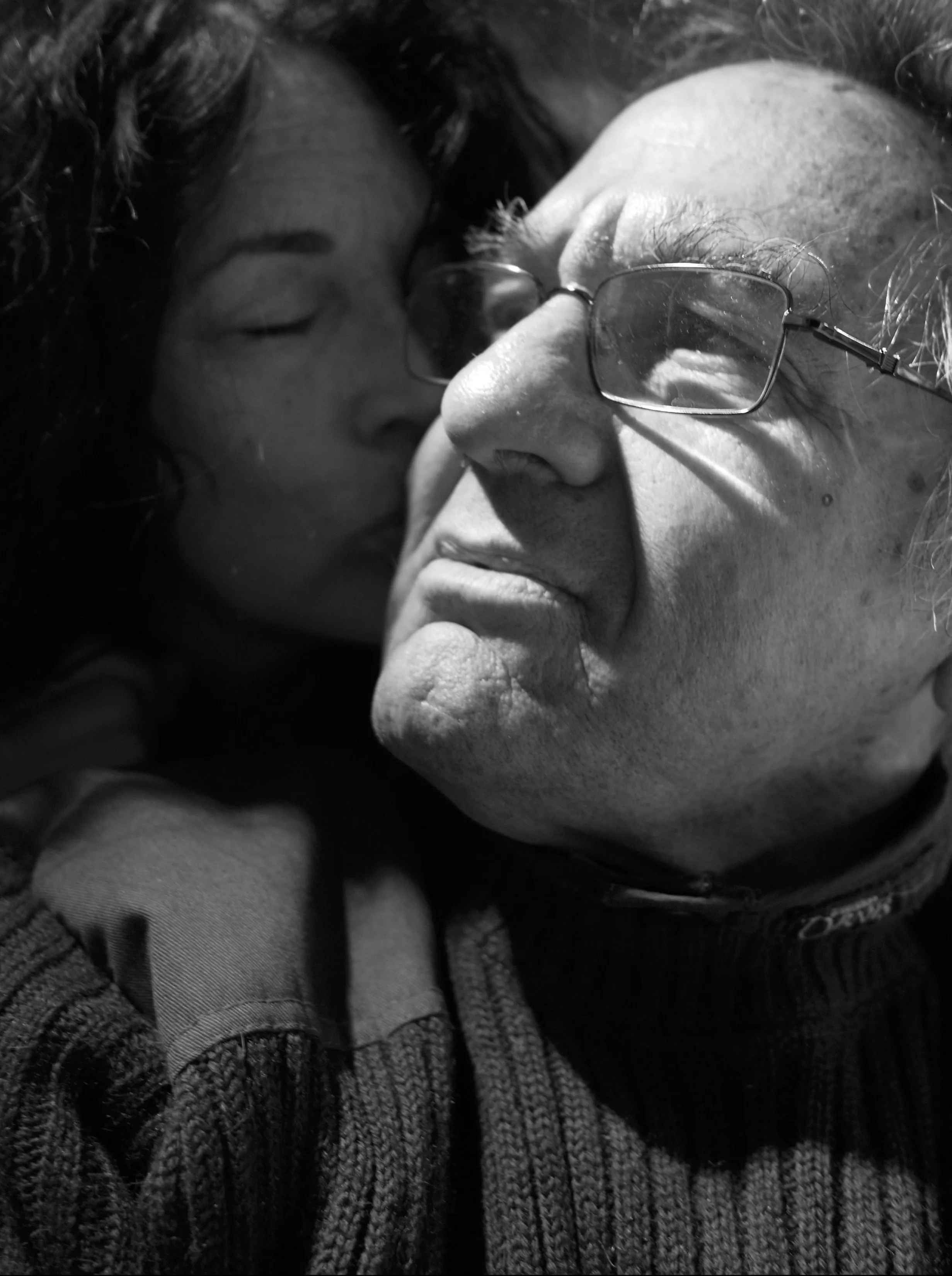 A lady giving a kiss on the cheek to an elderly man.