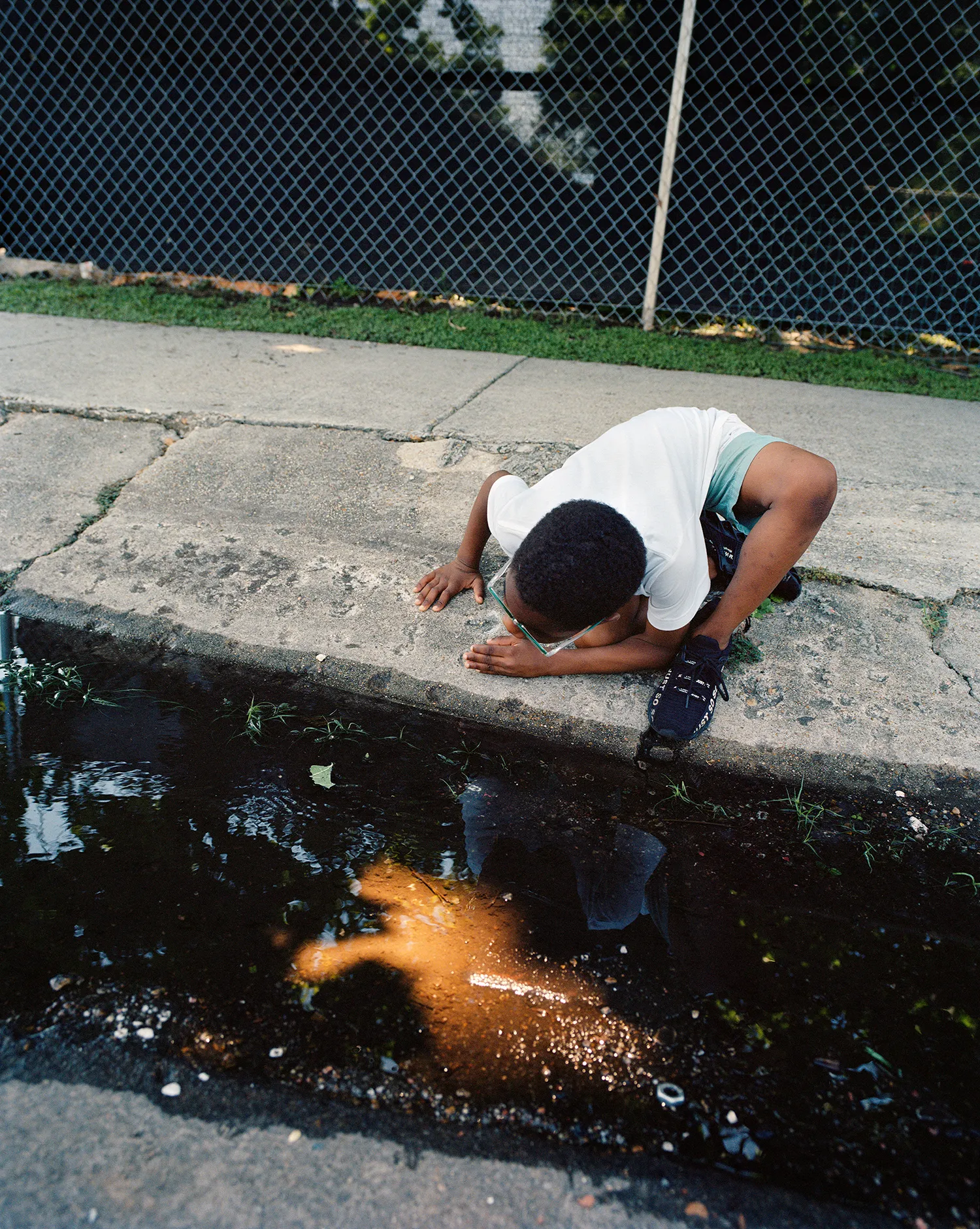 A young boy looking at the congealed goop on the side of the sidewalk. 